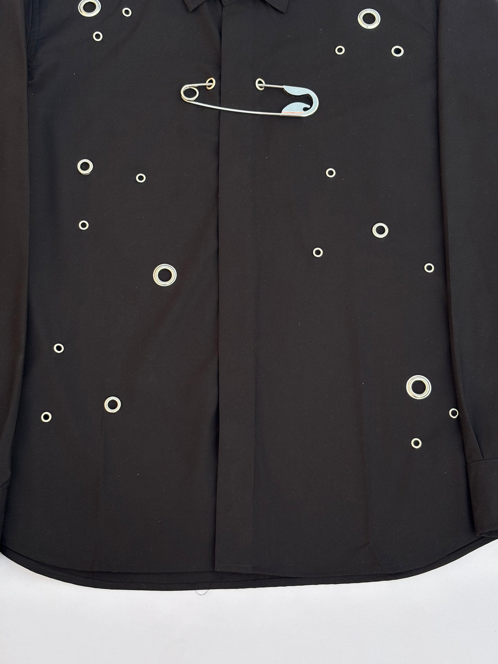 Black shirt with white buttons and a safety pin on a white background