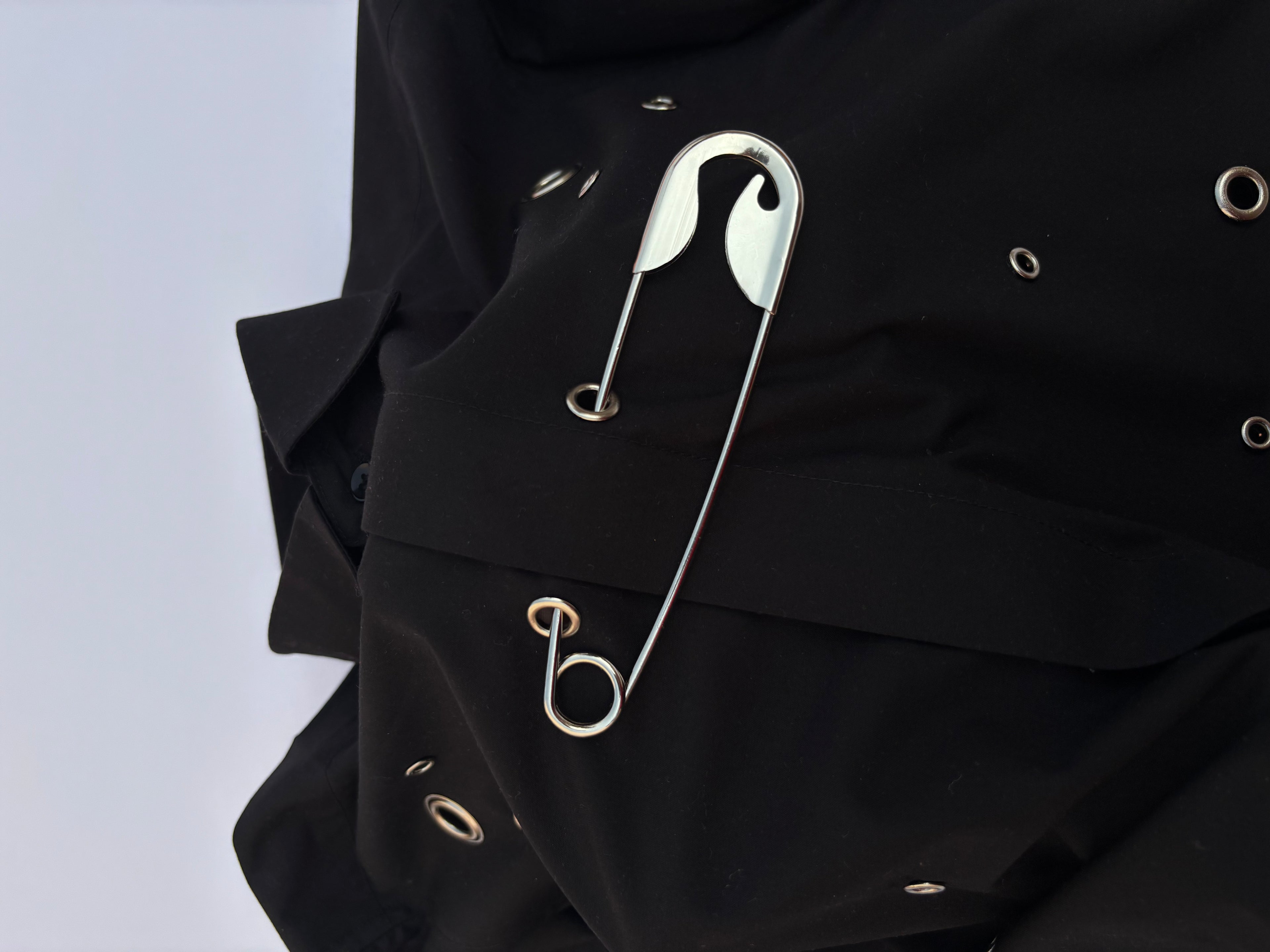 Close-up of a black garment with safety pins on a light purple background
