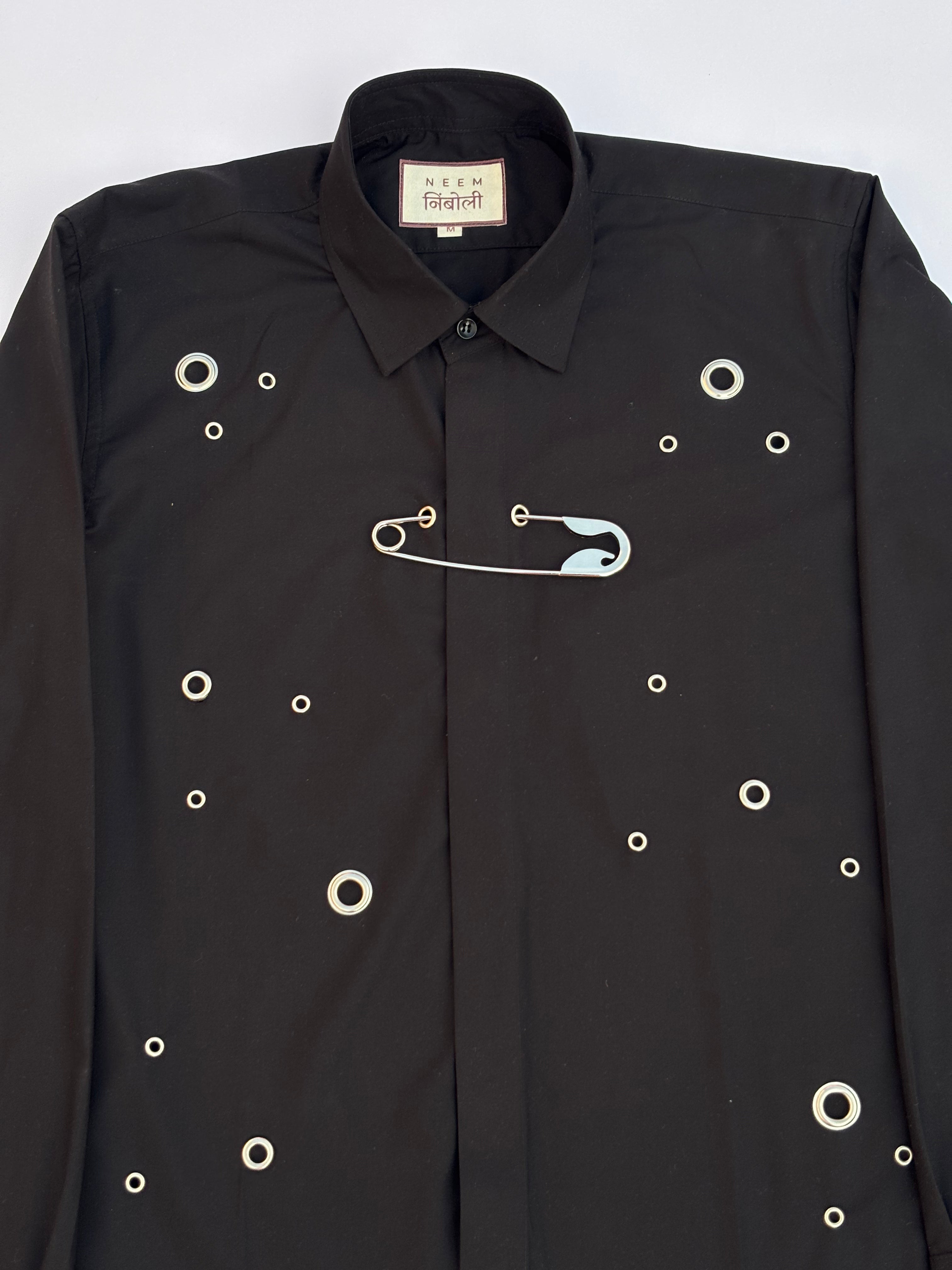 Black shirt with safety pin and eyelet design on a white background