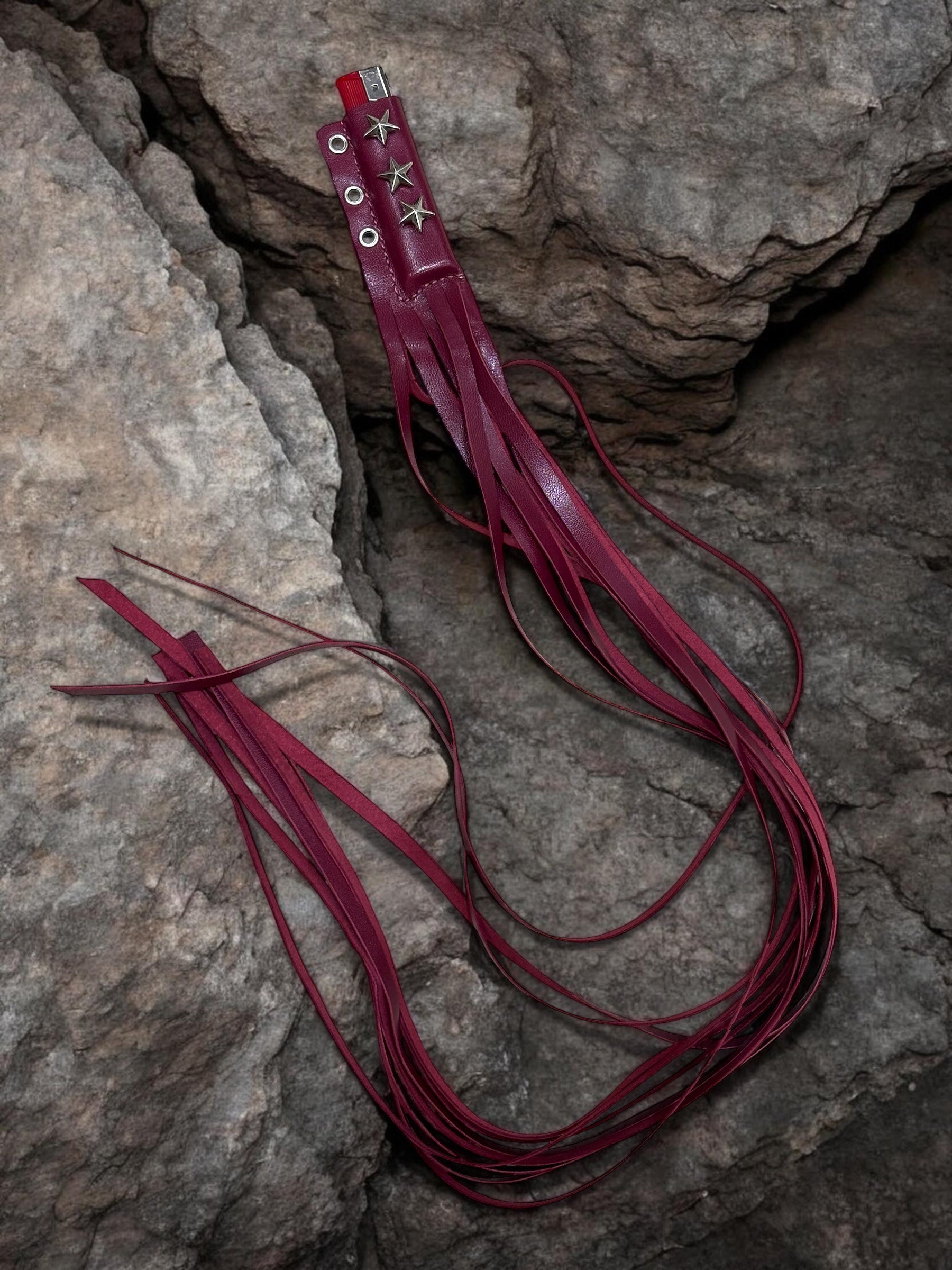 Red leather whip with decorative elements on a stone surface