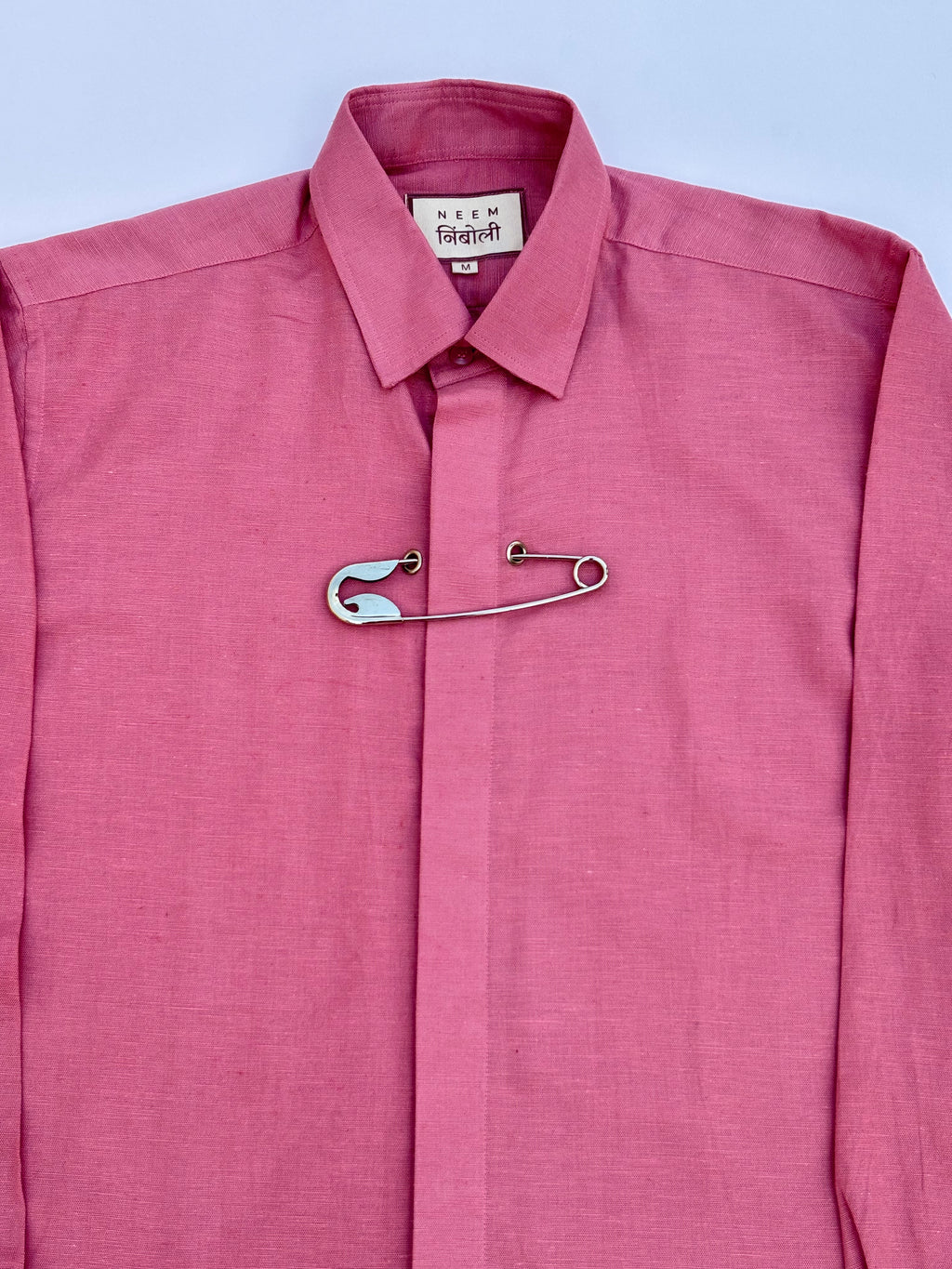 Pink shirt with a safety pin on a light blue background